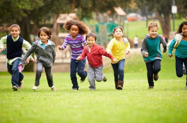 Group Of Young Children Running Towards Camera In Park Smiling