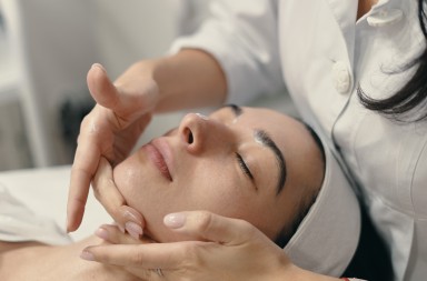 Beauty, spa and cosmetology concept. Young woman lies with closed eyes, cosmetologist making procedure for facial skin rejuvenation, facial massage.