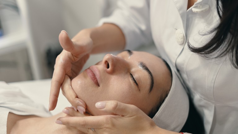 Beauty, spa and cosmetology concept. Young woman lies with closed eyes, cosmetologist making procedure for facial skin rejuvenation, facial massage.